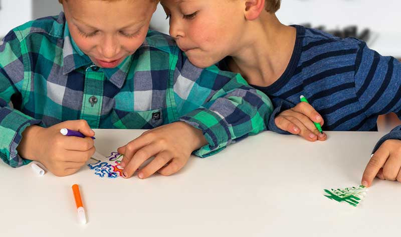 Two children sitting at a table coloring with markers.