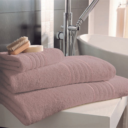 Stack of pink towels on a bathtub with a brush and soap dish in a bathroom setting.
